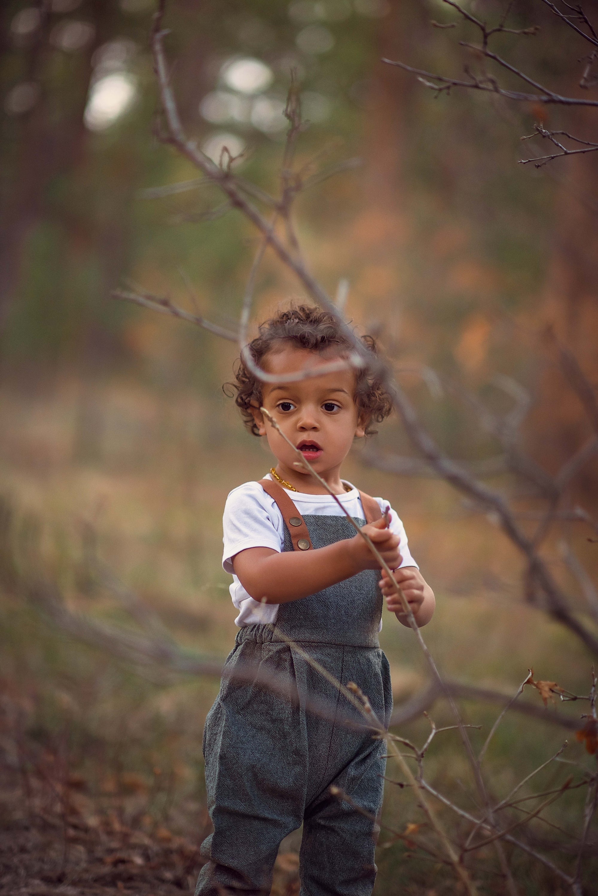 Child in overalls standing in a forest with blurred background