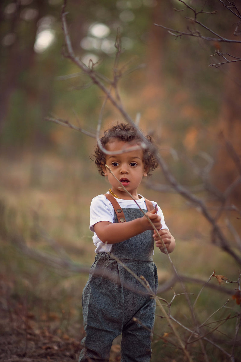 Child in overalls standing in a forest with blurred background