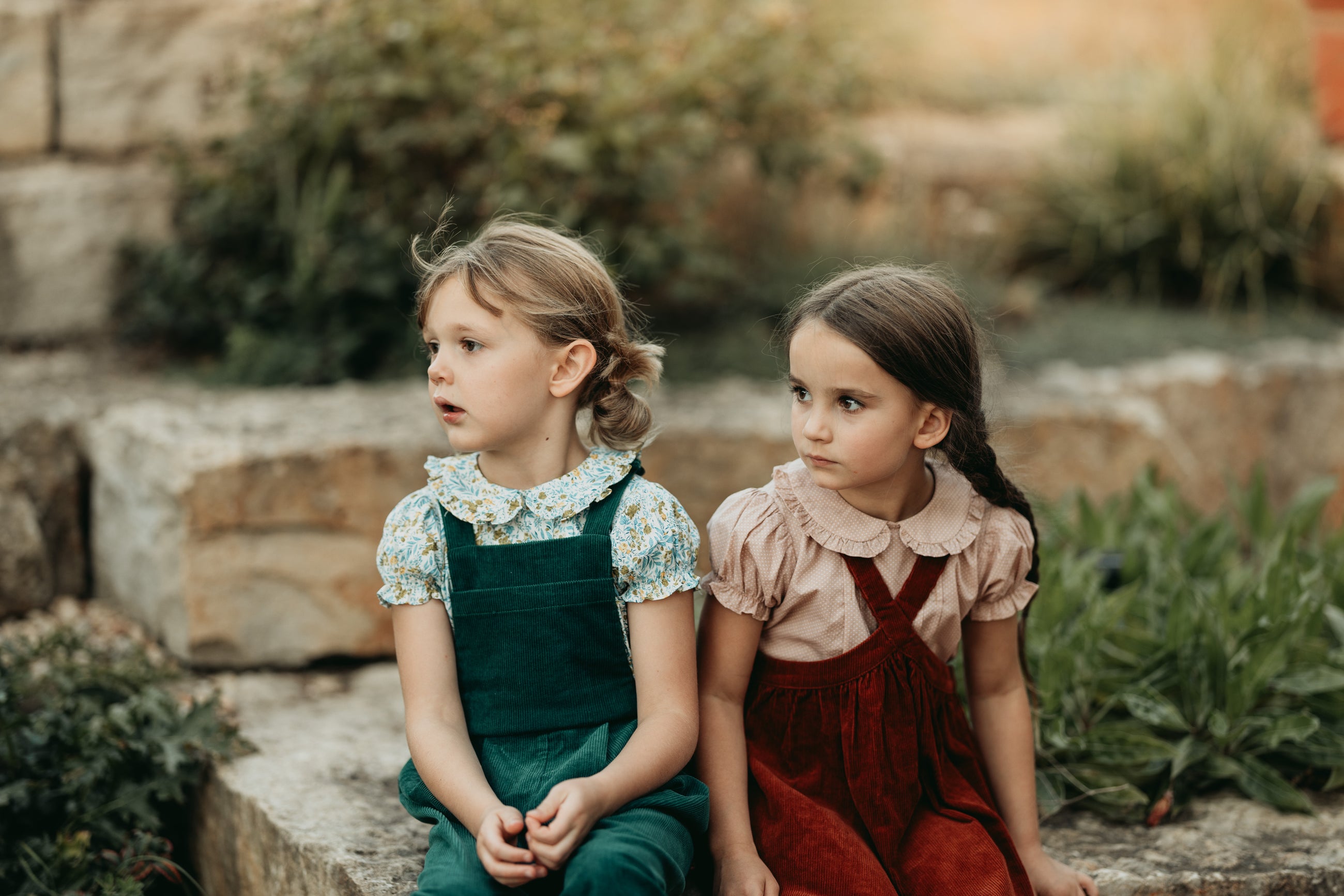Two young girls sitting on stone steps outdoors with a natural background
