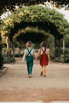 Two girls holding hands and walking away on a path with greenery around.