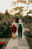 Two girls holding hands in a garden with pink flowers and greenery.