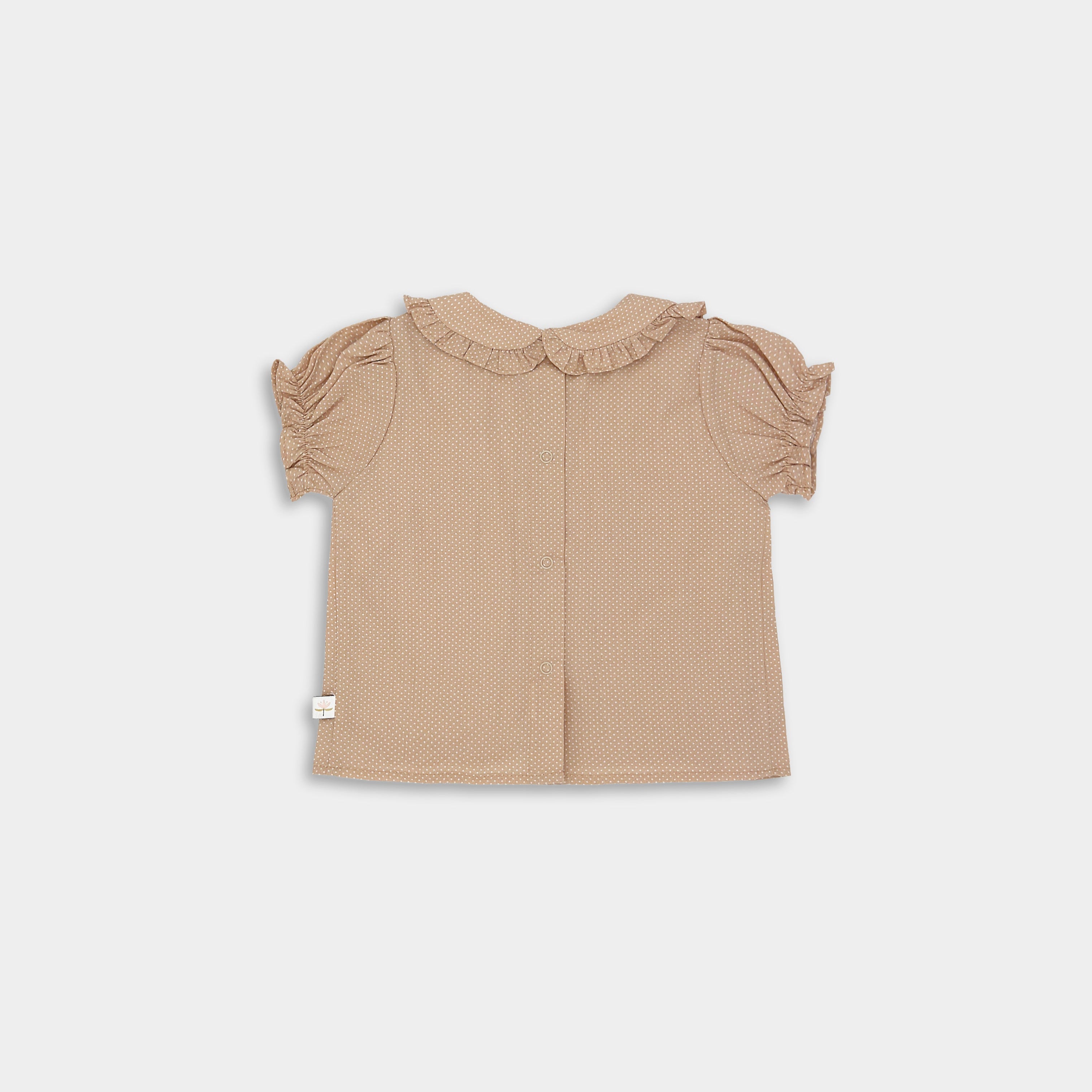 Back of beige blouse with white Swiss dots featuring a Peter Pan collar adorned with ruffles, short puffy sleeves with ruffled hems, and a snap closure at the back. Available in sizes 9-12 months to 5 years, made from natural pre-washed cotton for comfort.