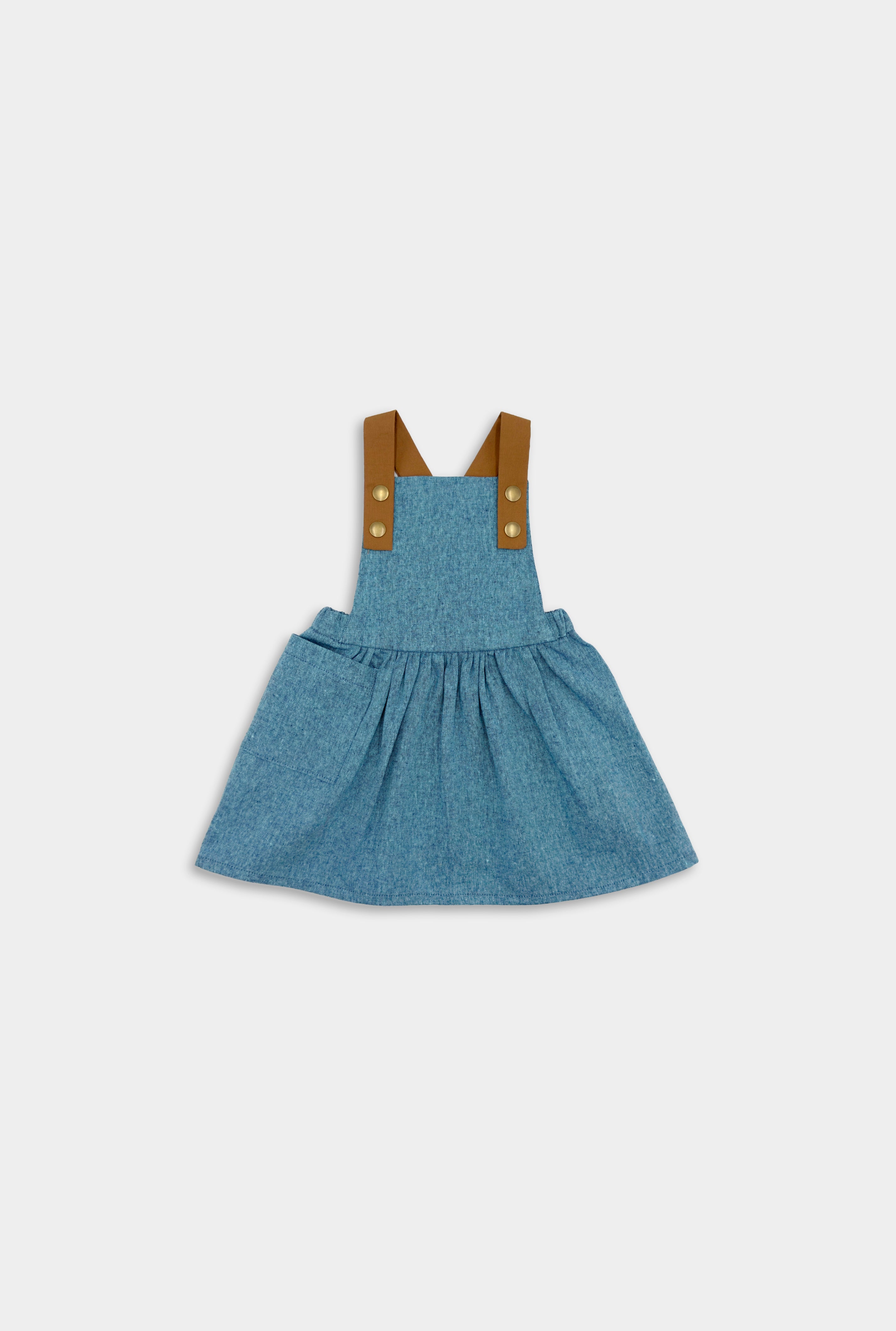 Pinafore in Blue Jay on a little girl model enjoying summer - This classic and timeless design is handmade in our NYC studio using repurposed linen. The pinafore is designed to be worn on its own, ensuring your little girl stays stylish and cool all summer long. Durable leather-looking straps enhance visual appeal, while adjustable straps in two lengths provide a perfect fit. The generous pocket is perfect for storing her little treasures during outdoor adventures.