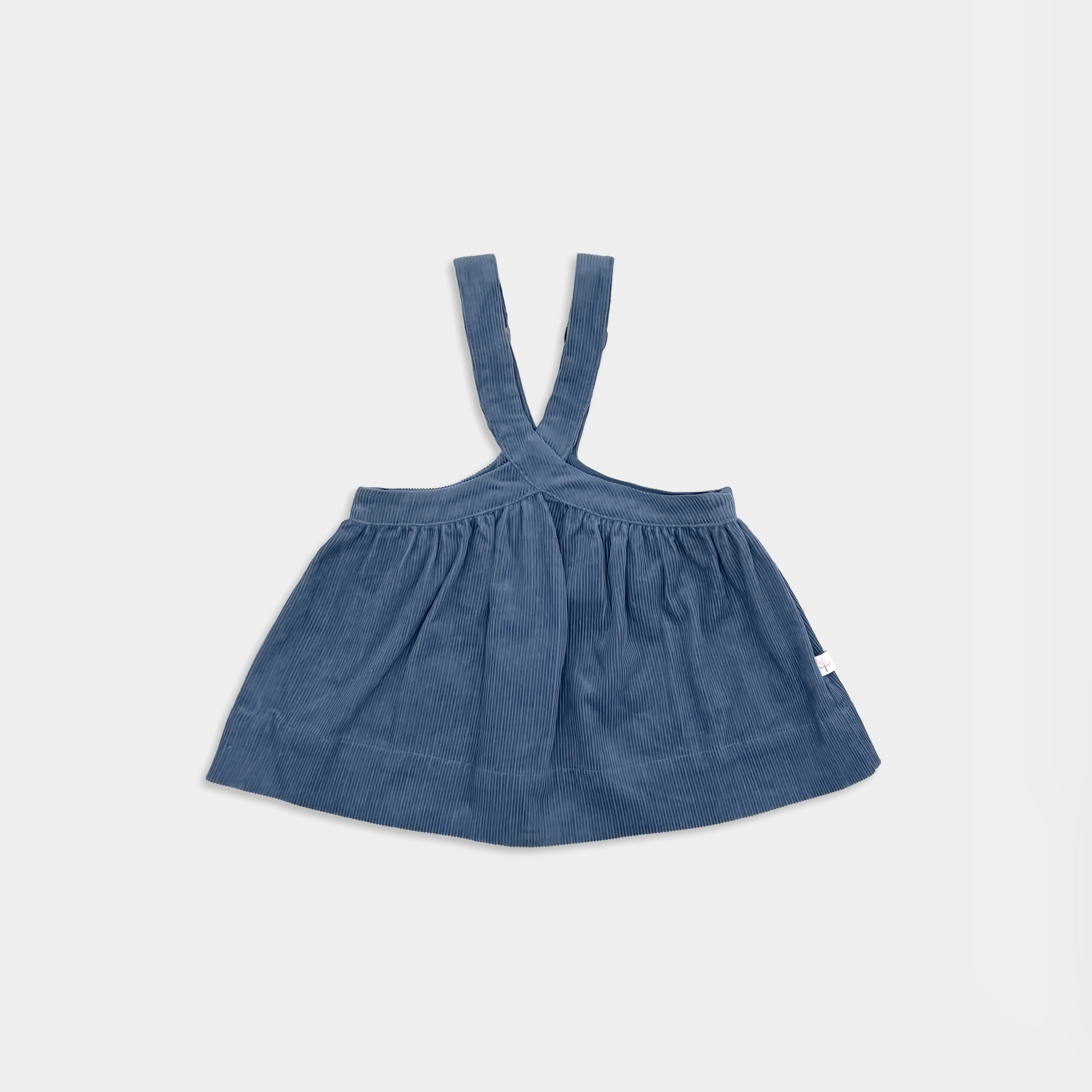 Front view of a blue corduroy pinafore with suspenders on a light gray background for small girls