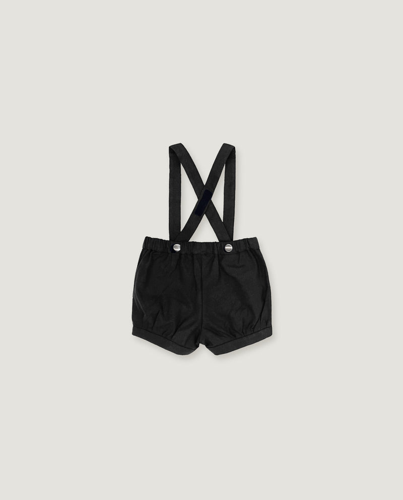Black baby boy's shorts with adjustable shoulder straps and silver snap buttons, laid flat on a light gray background.