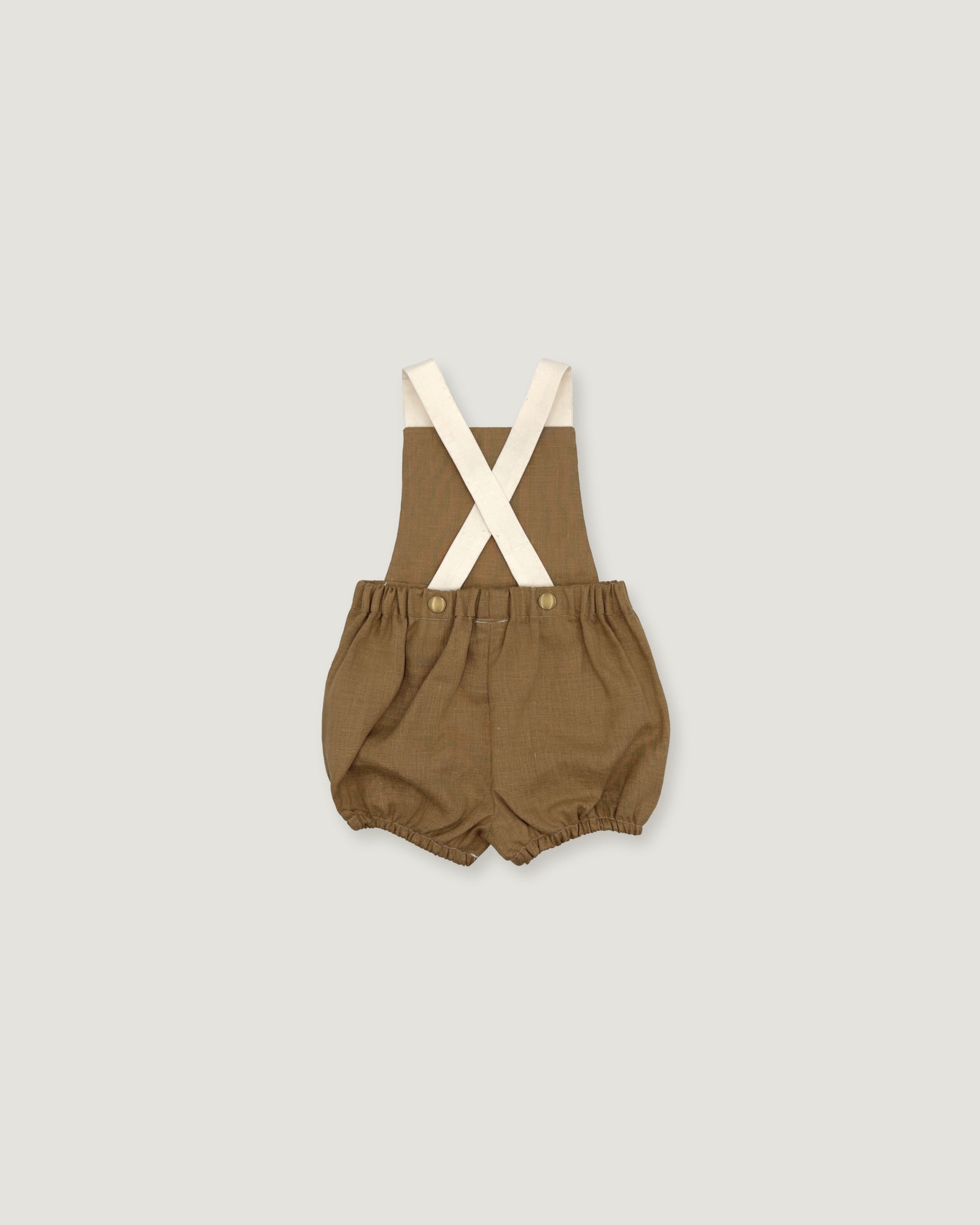 A baby romper in a warm brownish-olive fabric with cream-colored suspenders, laid flat against a light gray background.