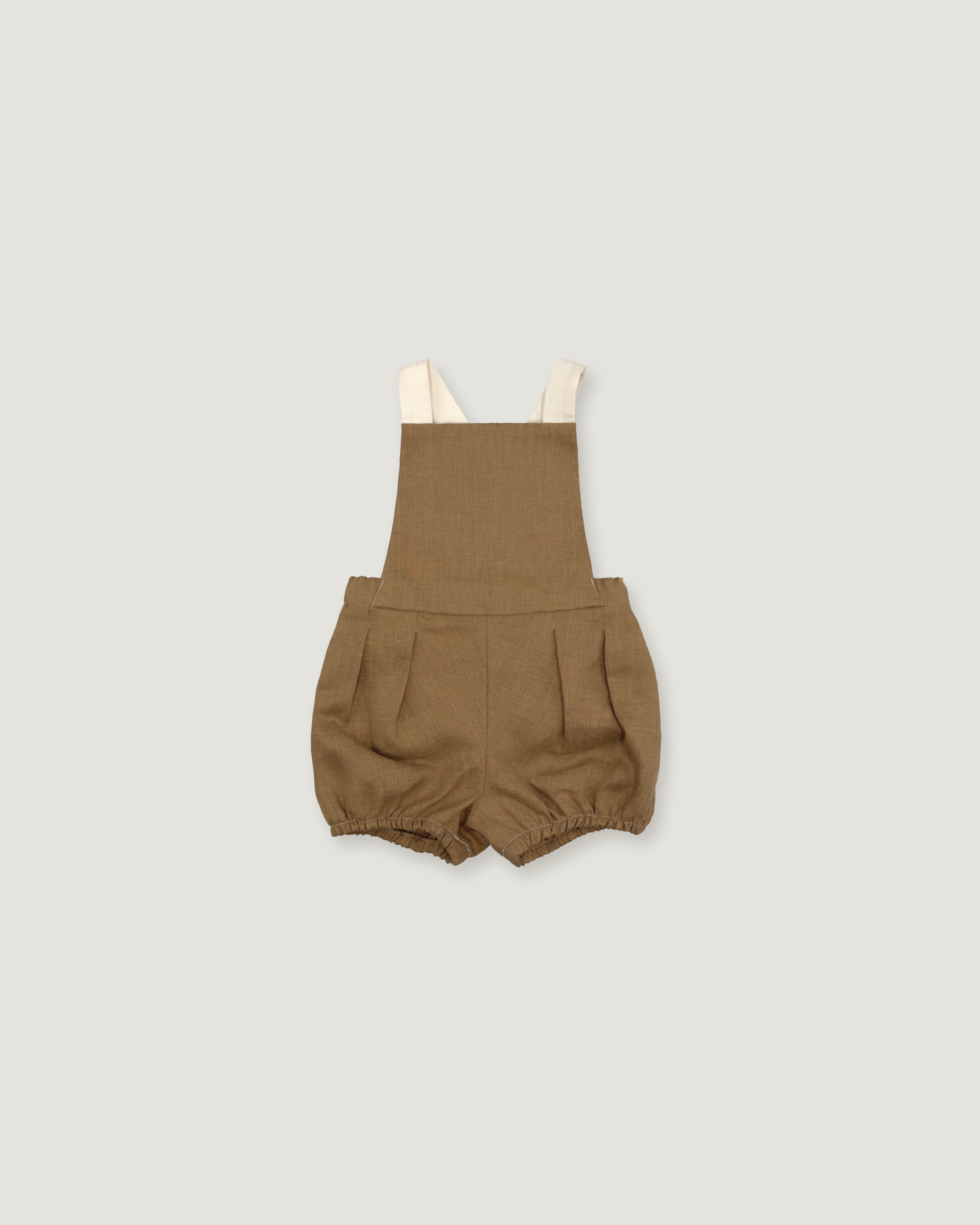 A pair of toddler's linen bubble shorts in a warm brownish-tan color, featuring adjustable cream-colored shoulder straps, shown flat on a light gray background.