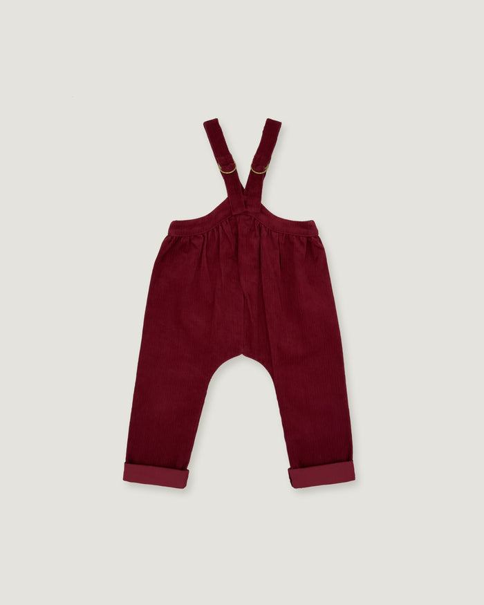 A pair of baby corduroy suspenders in deep burgundy, featuring adjustable shoulder straps and rolled cuffs, laid flat against a light gray background.