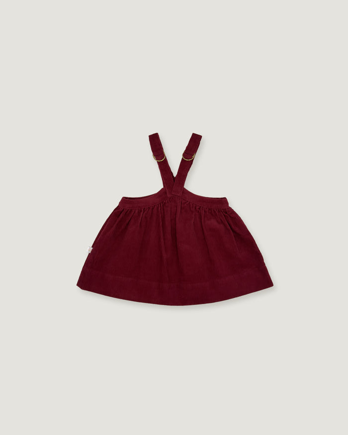 A dark burgundy baby girl's overall dress with adjustable shoulder straps, shown flat against a light gray background.