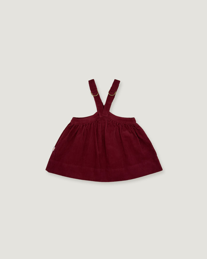 A dark burgundy baby girl's overall dress with adjustable shoulder straps, shown flat against a light gray background.