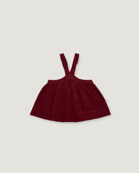 A dark burgundy baby dress with shoulder straps, laid flat against a light gray background.