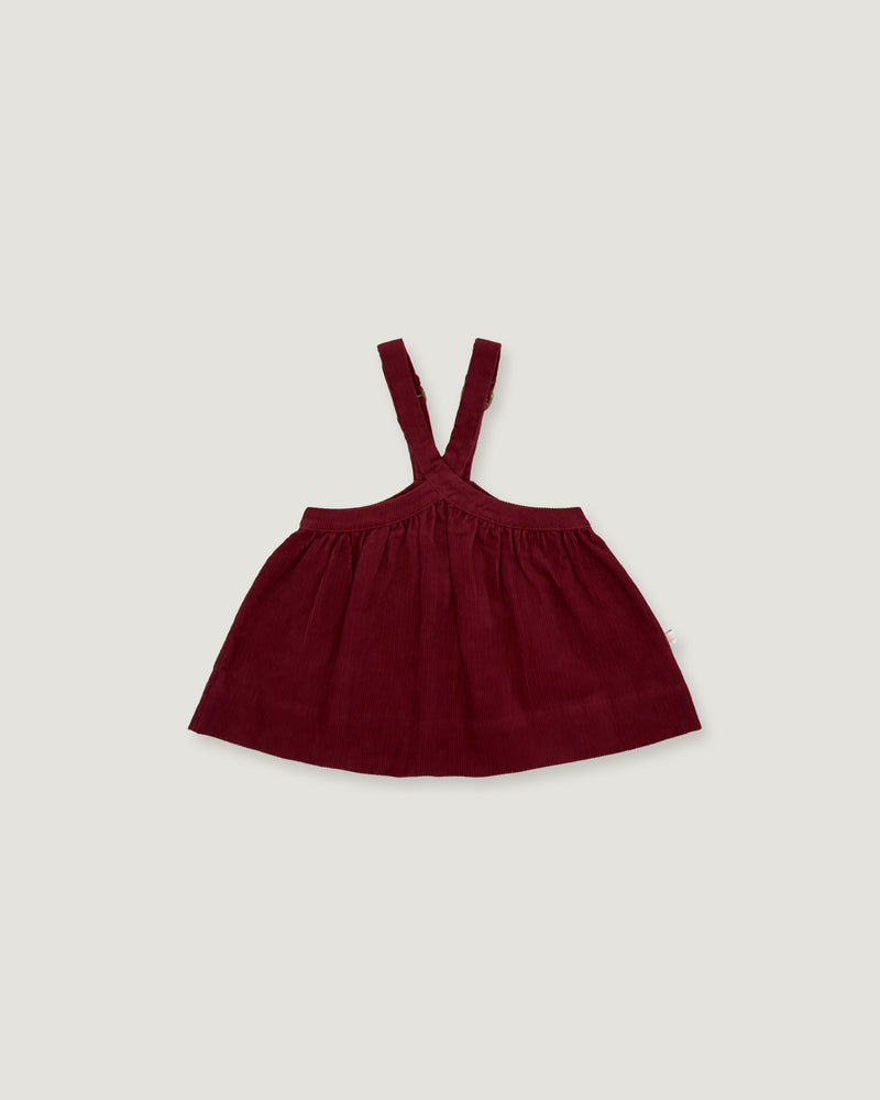 A dark burgundy baby dress with shoulder straps, laid flat against a light gray background.