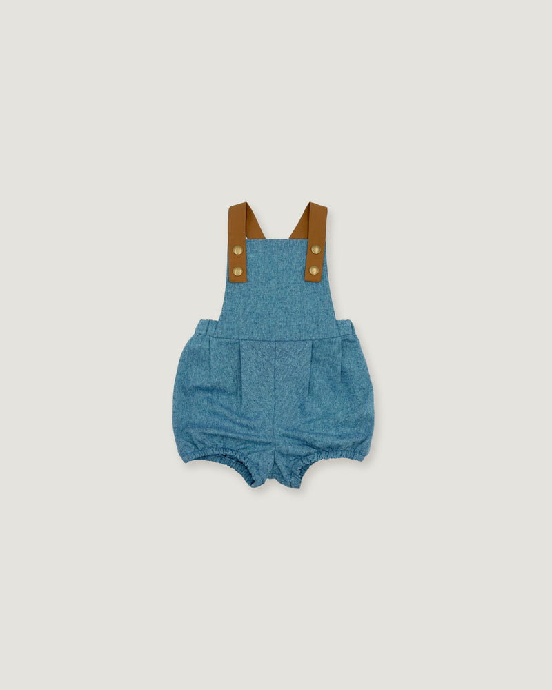 A baby romper in blue denim-like fabric with brown shoulder straps and gold-tone snap buttons, shown flat against a light gray background.