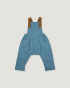A pair of baby blue denim overall-style pants with brown shoulder straps and brass-tone buttons, shown flat against a light gray background.