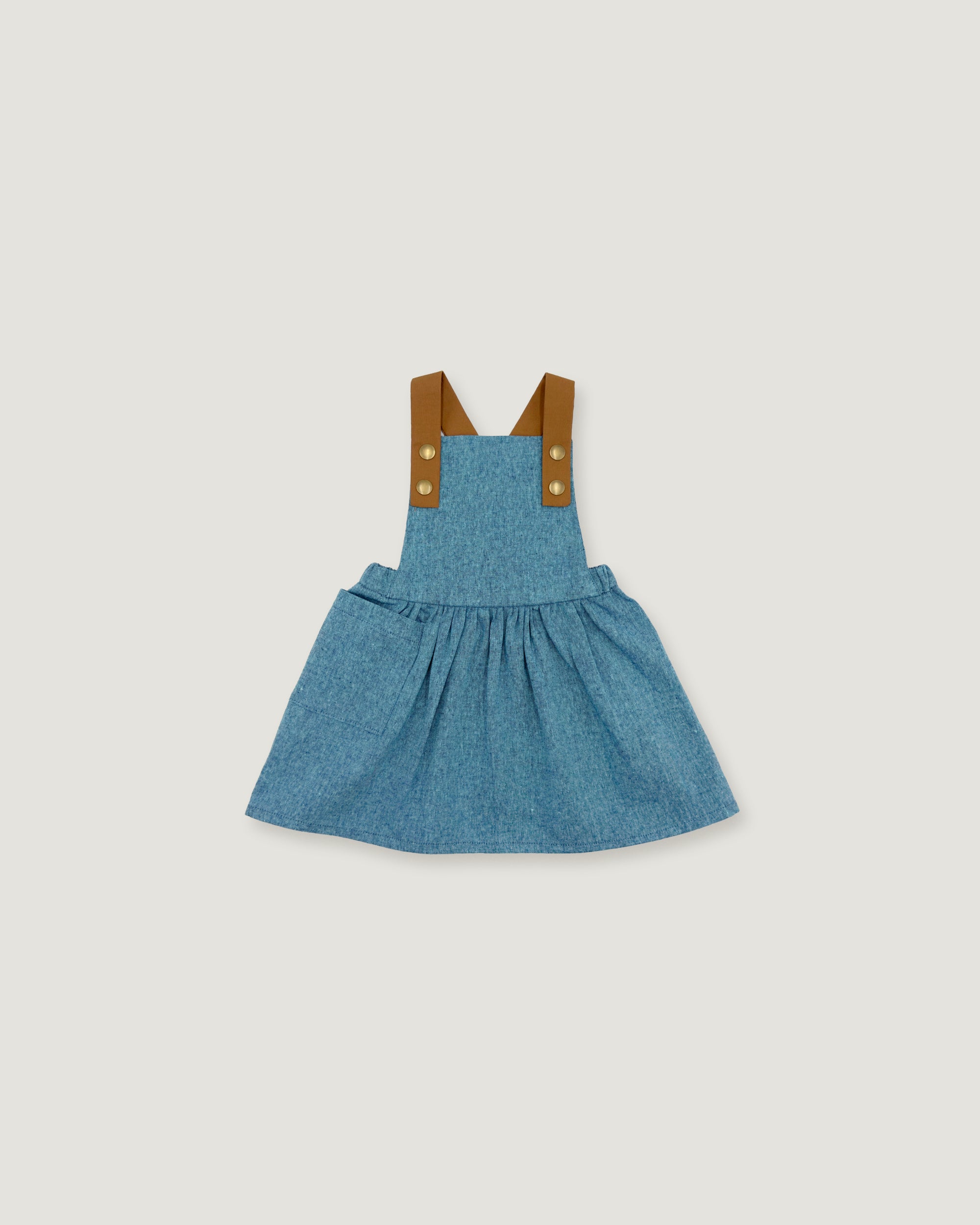 A toddler girl's blue denim overall dress with brown fabric shoulder straps and gold-tone buttons, shown flat on a light gray background.