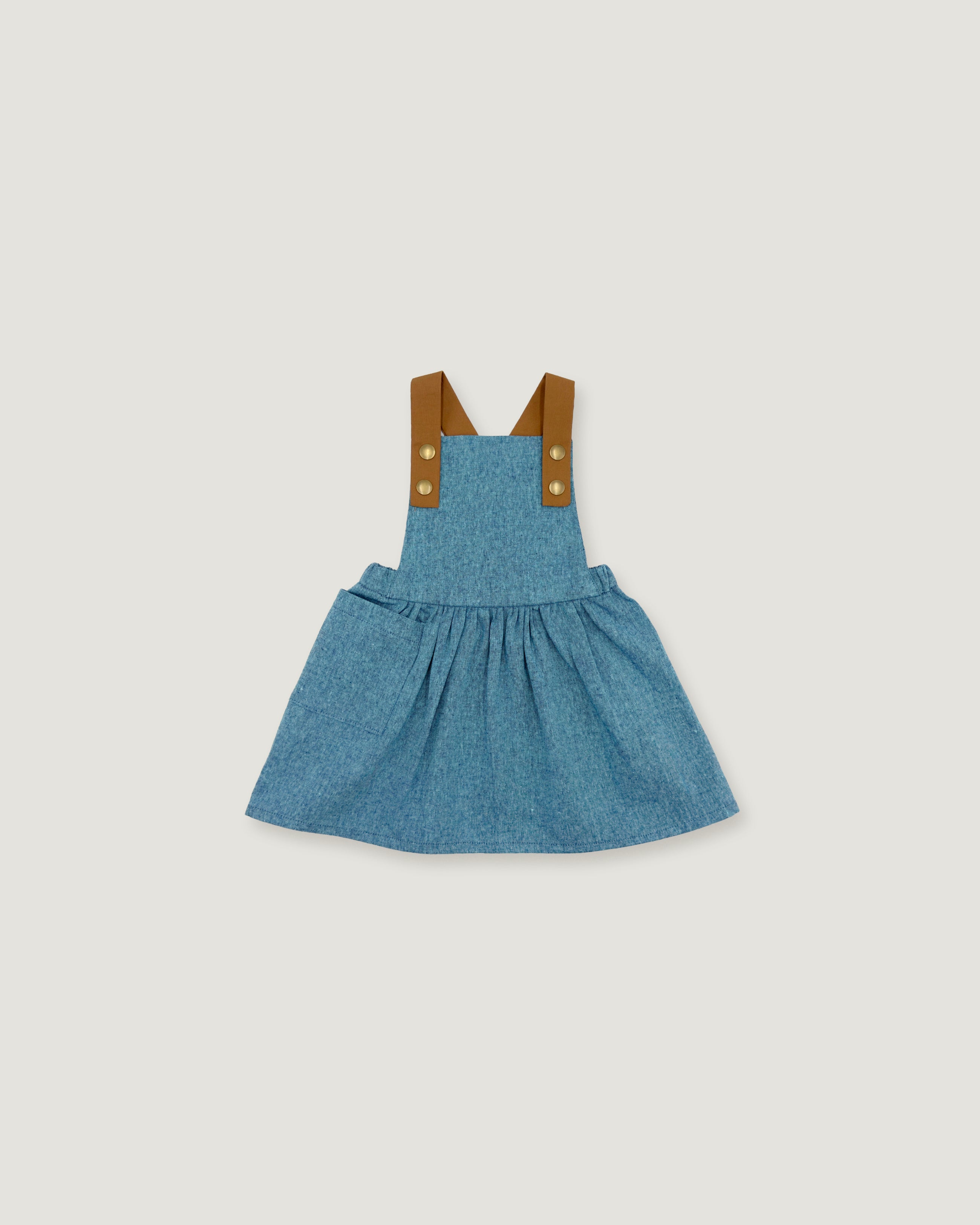A toddler girl's blue denim overall dress with brown fabric shoulder straps and gold-tone buttons, shown flat on a light gray background.