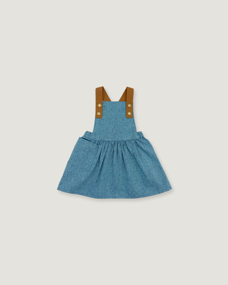 A toddler girl's blue denim overall dress with brown fabric shoulder straps and gold-tone buttons, shown flat on a light gray background.
