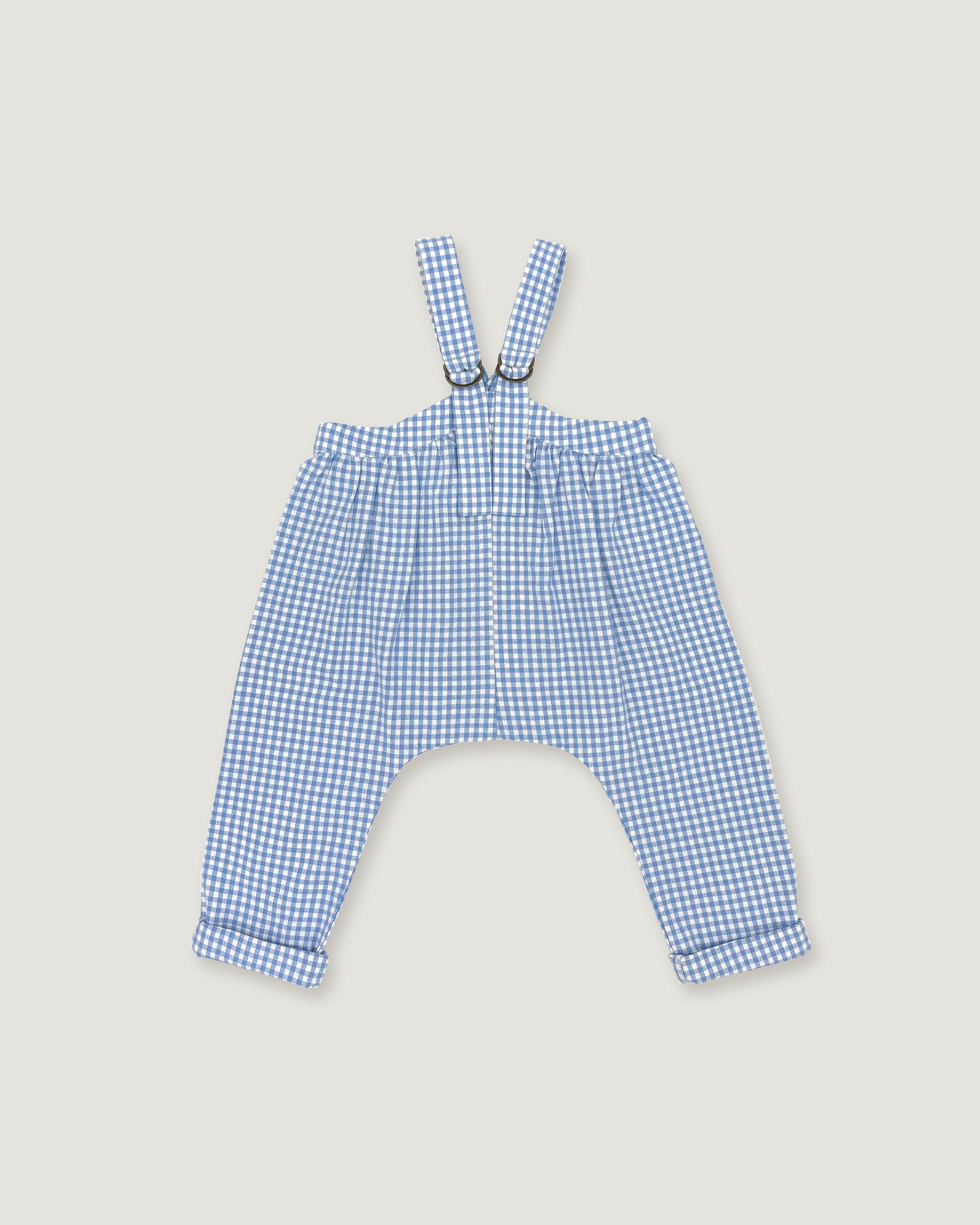 A pair of baby boy's blue and white gingham check suspenders with adjustable straps and a drawstring waist, laid flat on a light beige background.