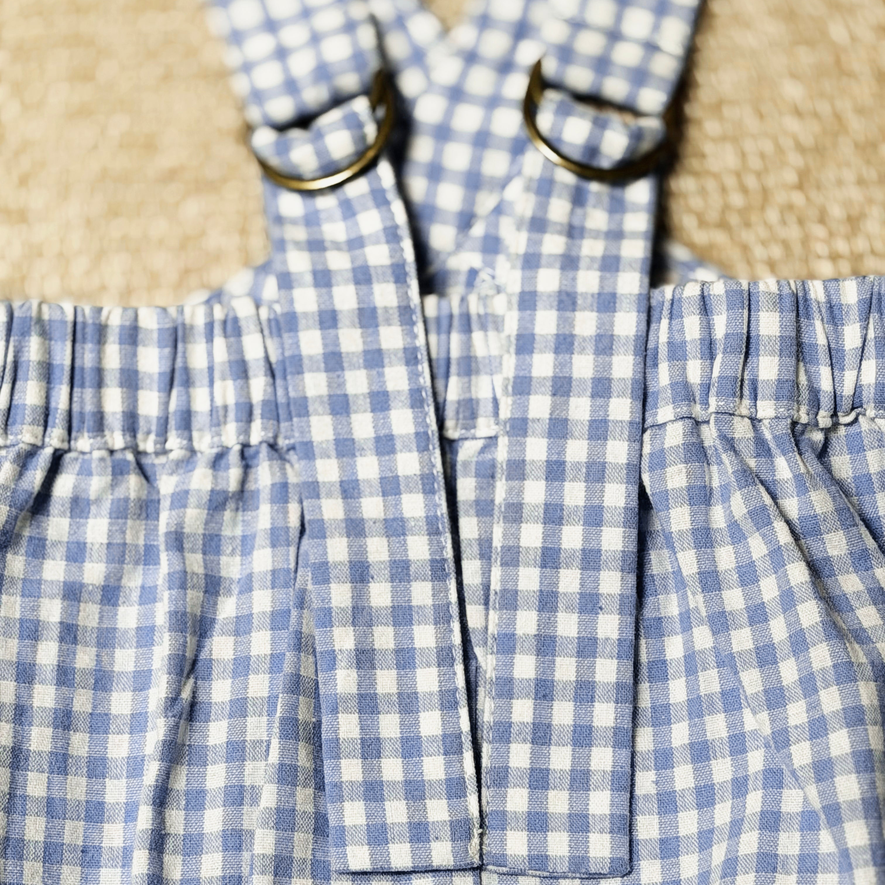 Close-up of a blue and white checkered dress with straps on a textured beige background
