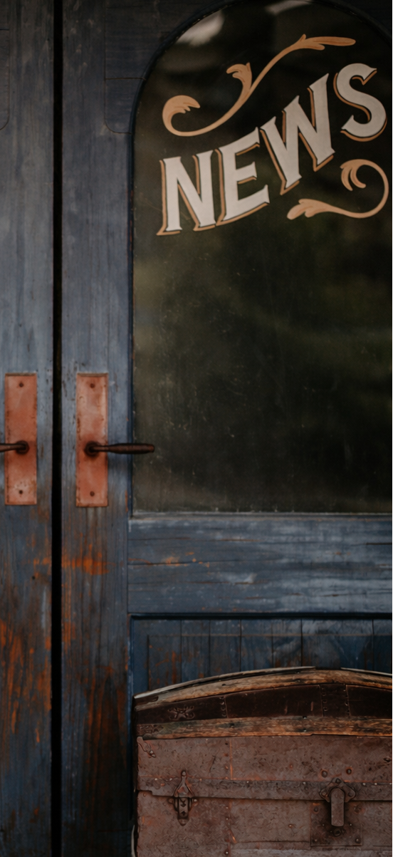 Vintage wooden doors with 'Daily News' sign and old wooden chest in front.