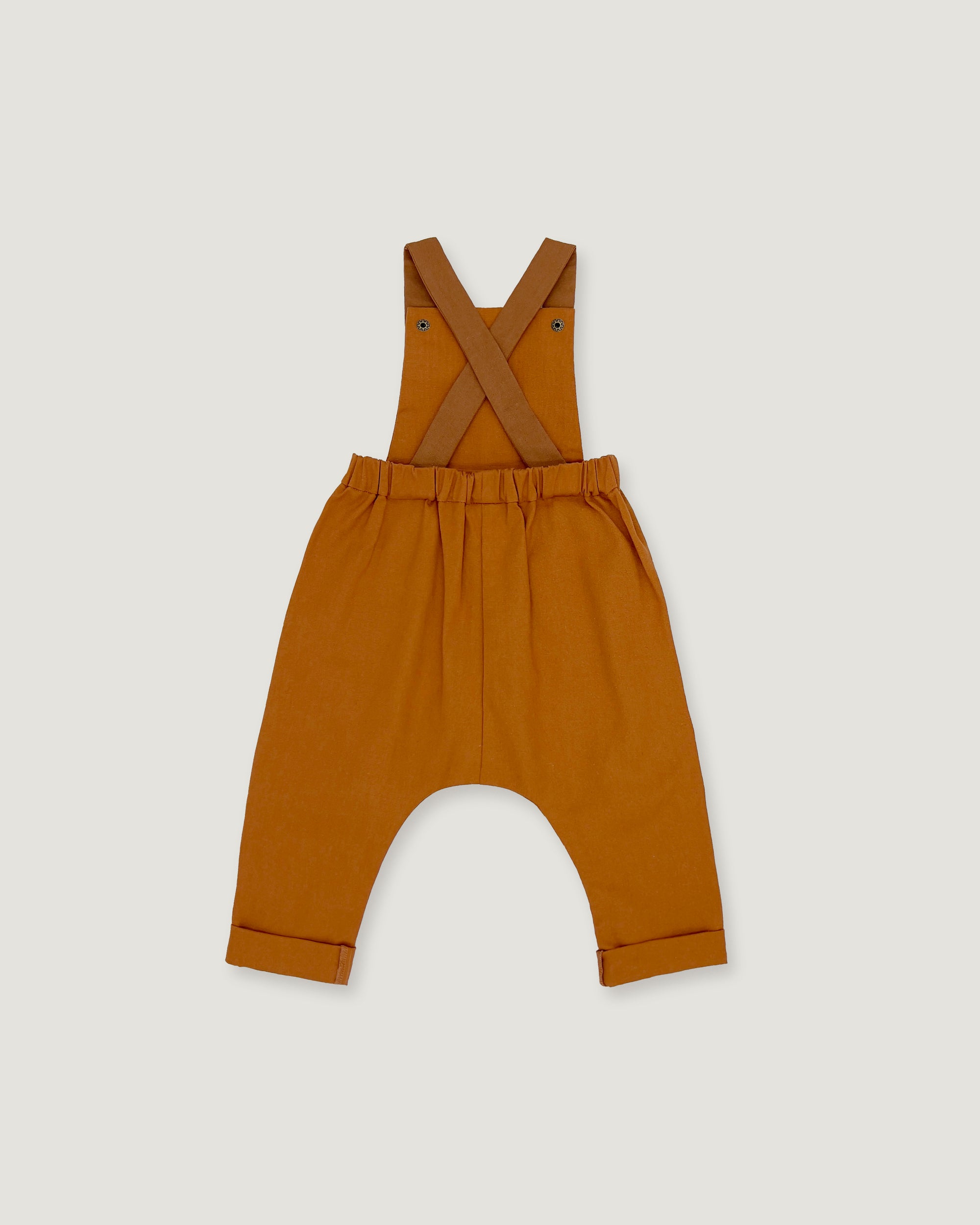 A pair of rust baby overalls with adjustable shoulder straps and a wide leg, laid flat on a light gray background.