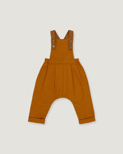 A pair of rust baby overalls with adjustable shoulder straps and a wide leg, laid flat on a light gray background.