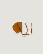 A rusty orange brown bonnet with a long visor and with adjustable tie straps, displayed flat against a light gray background.