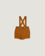A pair of toddler's short trousers in a warm camel brown color, featuring adjustable shoulder straps that cross over at the back and snap button closures at the waist, displayed flat against a light gray background.