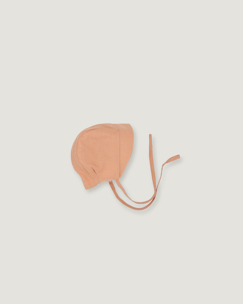 A peach-colored fabric bonnet with adjustable ties, photographed flat against a light gray background.