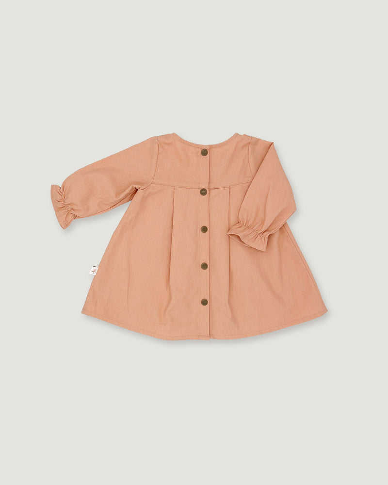 A peach-colored long-sleeve baby dress with gathered ruffled cuffs and a front button closure, displayed flat against a light gray background.