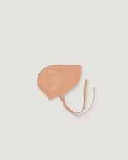 A light peach-beige bonnet-style with adjustable tie strings, shown flat against a solid light gray background.