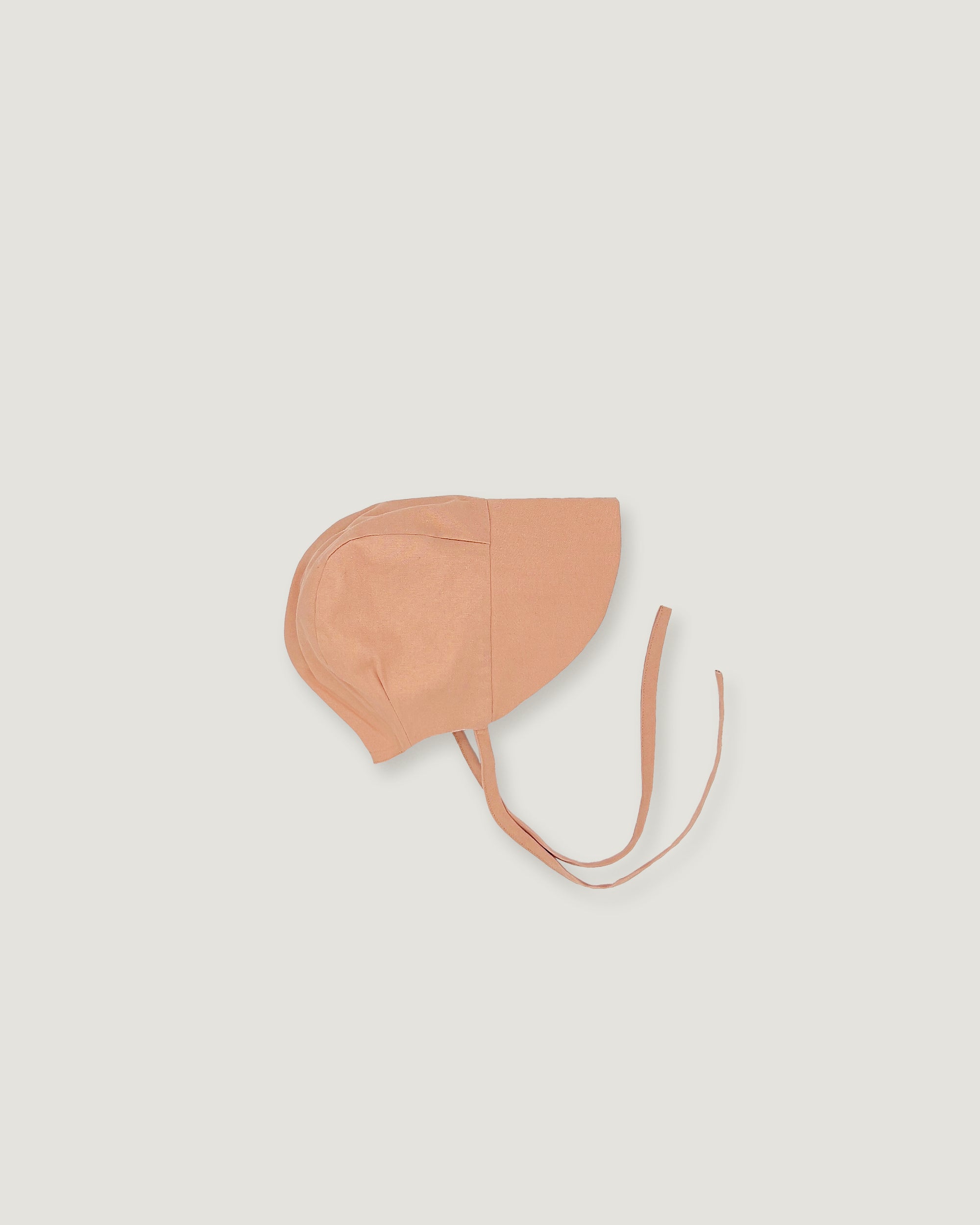 A light peach-beige bonnet-style with adjustable tie strings, shown flat against a solid light gray background.