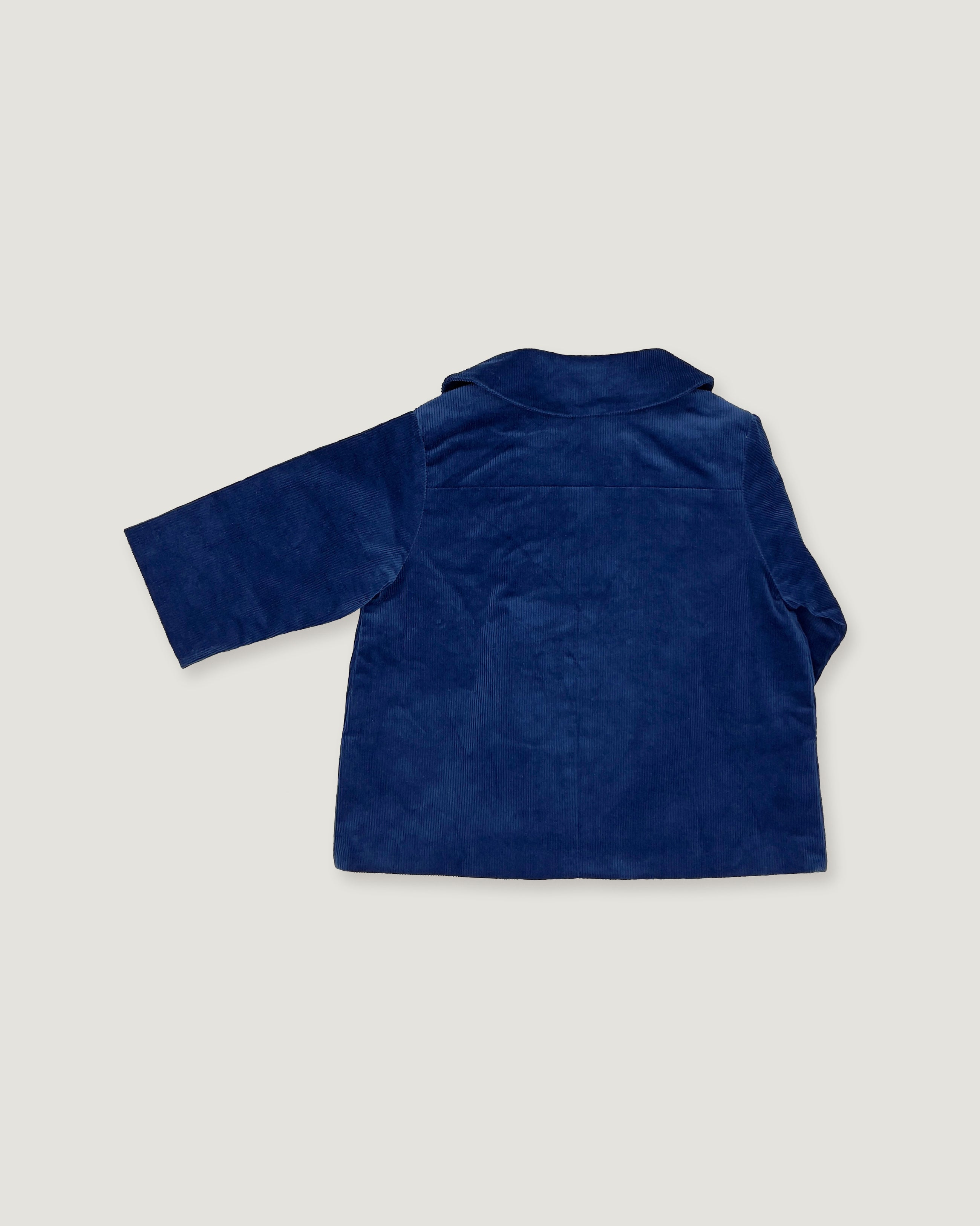 The back view of a navy blue corduroy jacket for a toddler, featuring a double-breasted design with gold buttons, a pointed collar, and front patch pockets, shown against a light gray background.