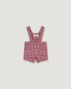 A baby romper in a red and white gingham check pattern, featuring adjustable shoulder straps and front patch pockets, displayed flat against a light gray background.