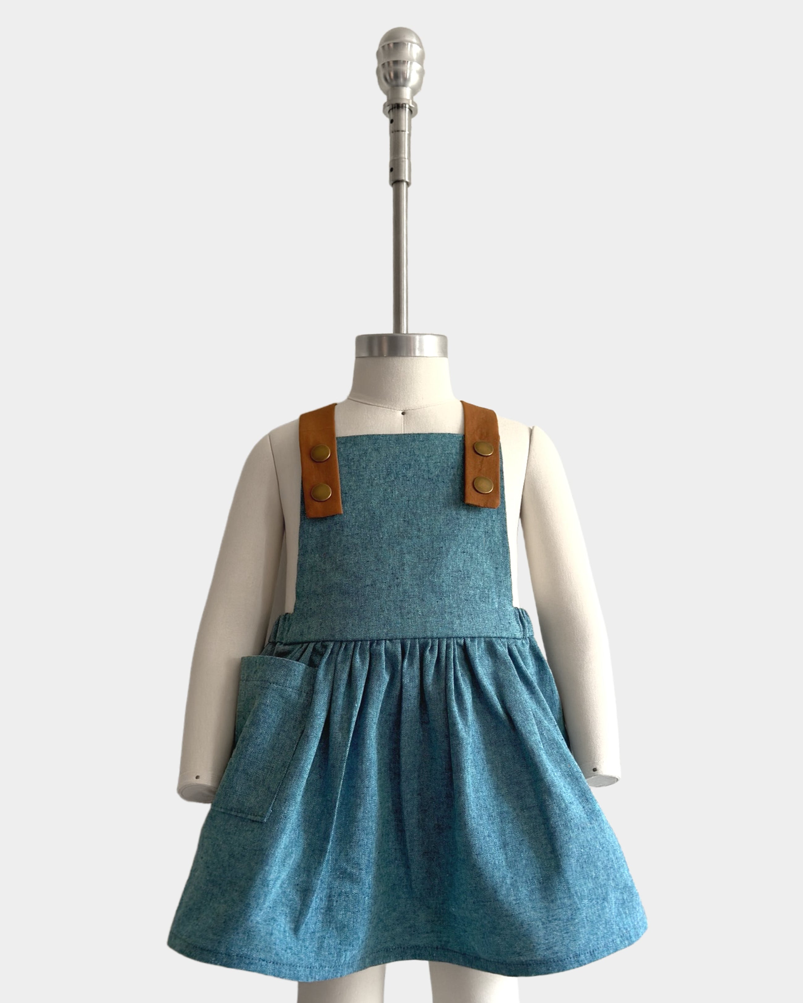 The Blue Jay pinafore displayed on a mannequin to showcase its perfect fit - Handmade from repurposed linen in our NYC studio, this classic design features durable leather-looking straps and adjustable lengths for an ideal silhouette. The generous pocket adds functionality while maintaining a stylish look, making it a versatile choice for summer wear.