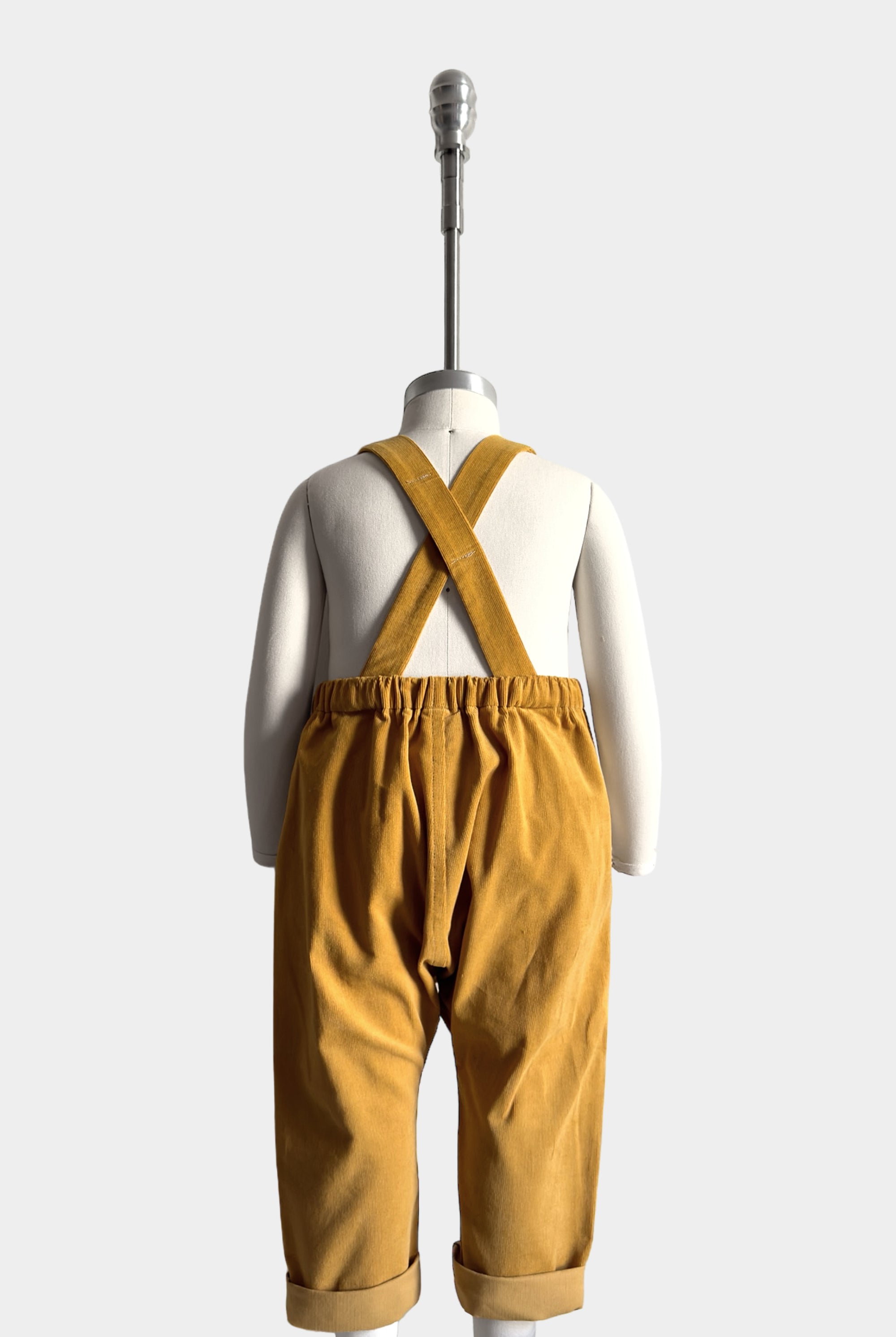 Back view of the mannequin in the overalls, showcasing the adjustable straps and overall construction. Adjustable straps stay up thanks to the strategically placed label. Elasticized back for comfort and best fit.