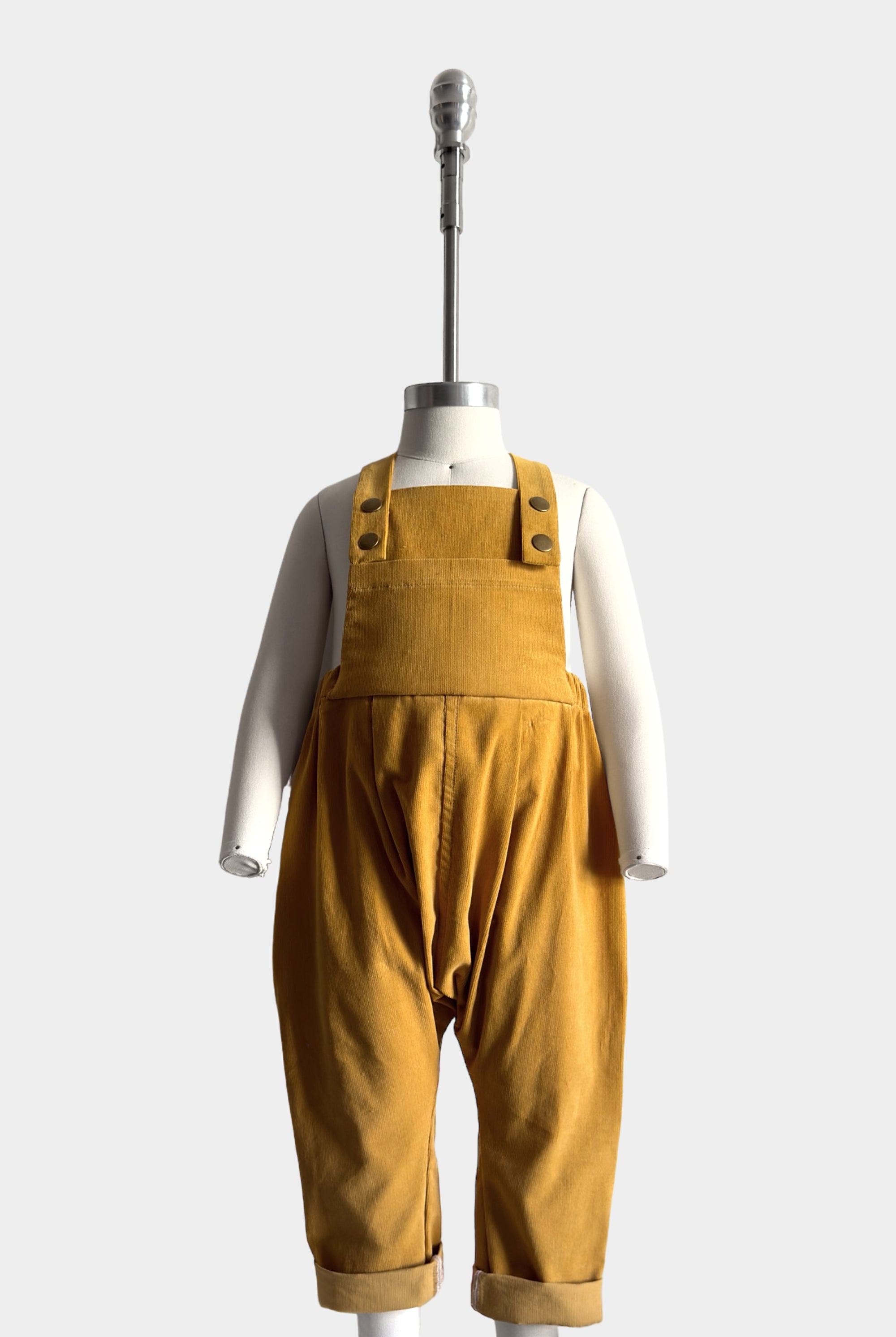 Mannequin wearing the Ginger Corduroy overalls front view, displaying the overall fit and design details including pleats, snap closures and oversized bib pocket.
