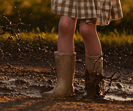 Person wearing checkered skirt and rain boots splashing in a muddy puddle