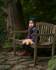 A 4-year-old boy sitting on a bench while wearing the cornflower indigo blue corduroy bonnet, highlighting its timeless accessory appeal and comfort for everyday wear.