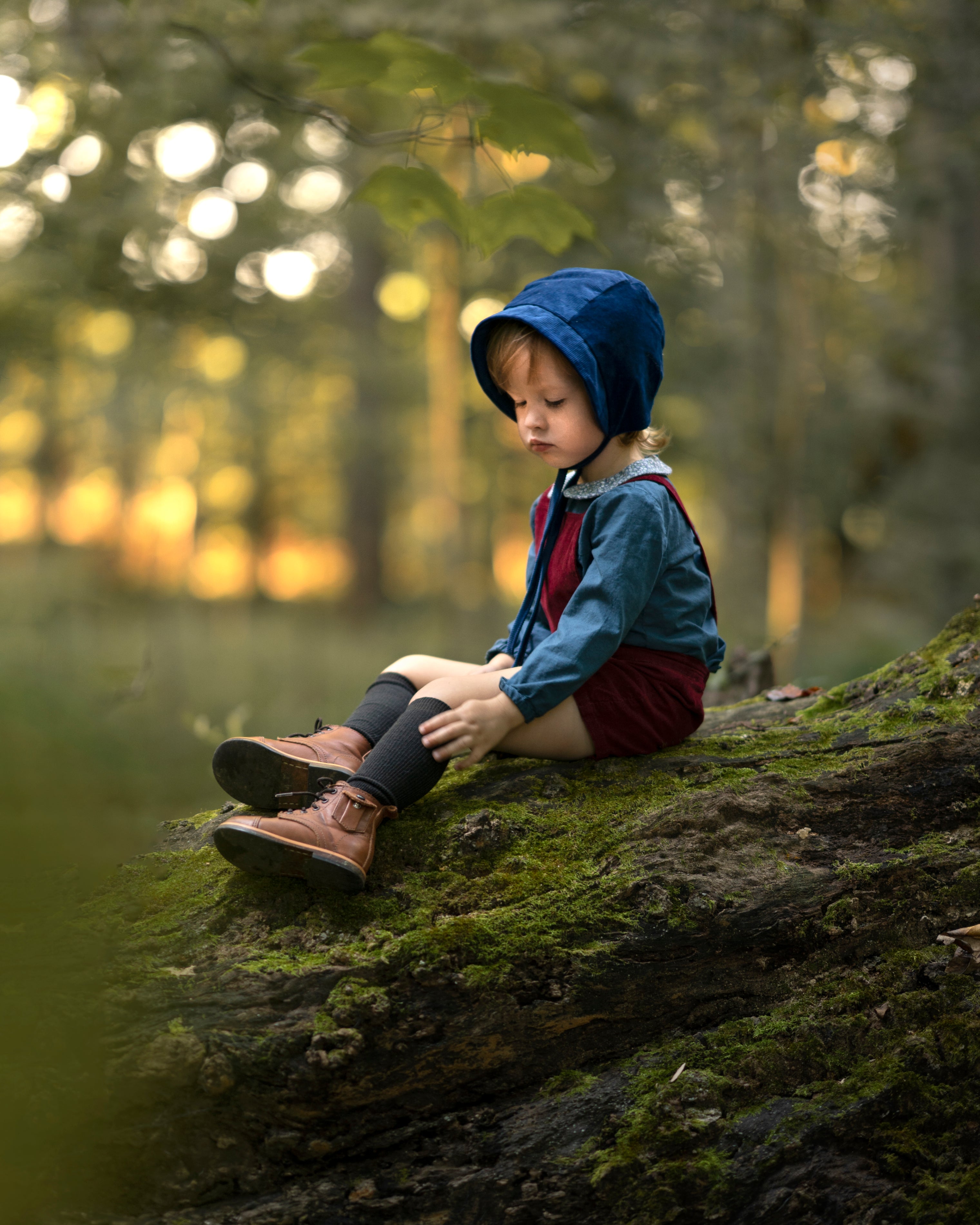 A 4-year-old boy sitting down, wearing the cornflower indigo blue corduroy bonnet, showcasing its adorable look and gender-neutral style suitable for all children.