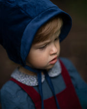 Close-up of a 4-year-old boy’s face wearing the cornflower indigo blue corduroy bonnet, emphasizing the comfort and warmth provided by the fully lined brushed gingham cotton.