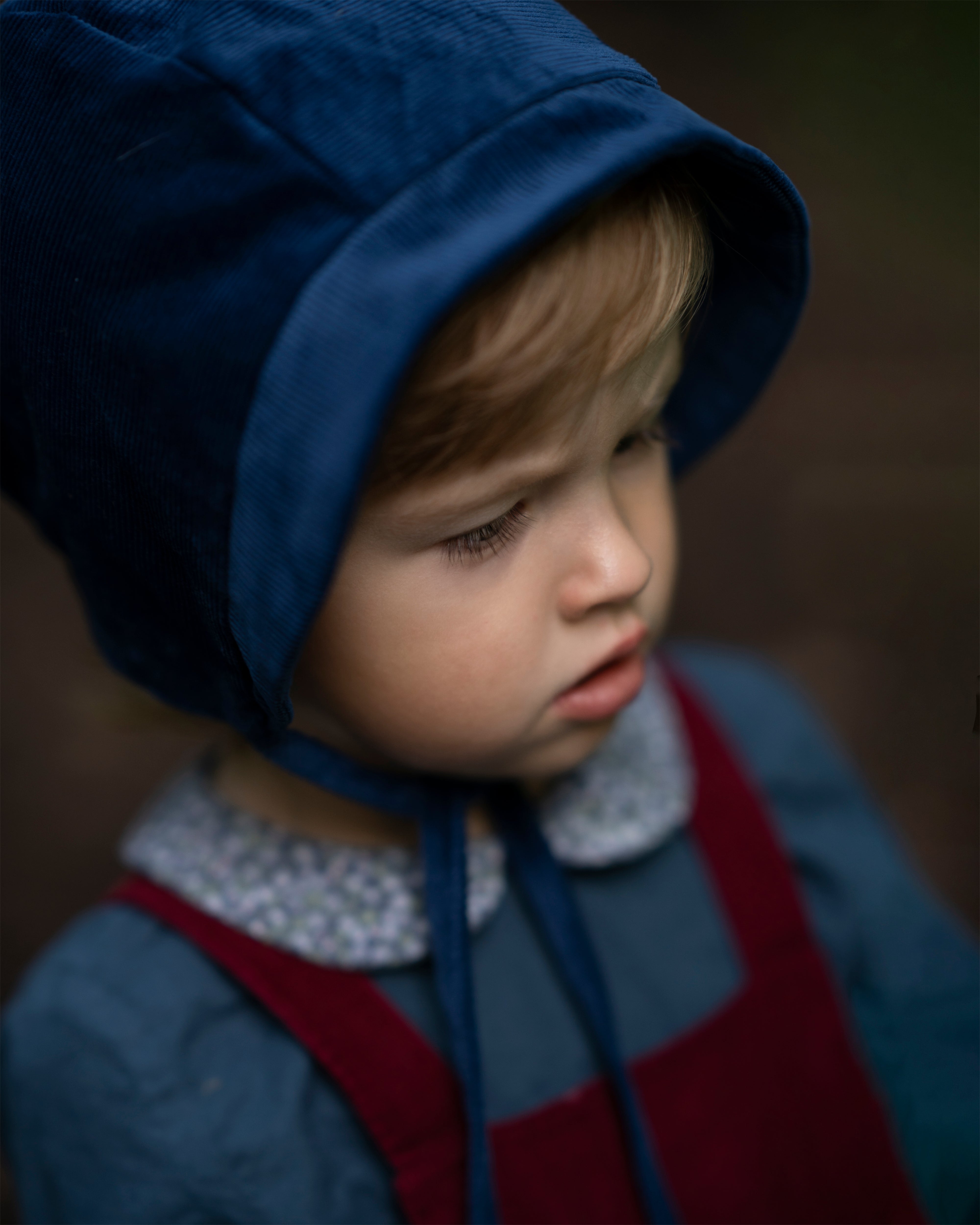 Close-up of a 4-year-old boy’s face wearing the cornflower indigo blue corduroy bonnet, emphasizing the comfort and warmth provided by the fully lined brushed gingham cotton.