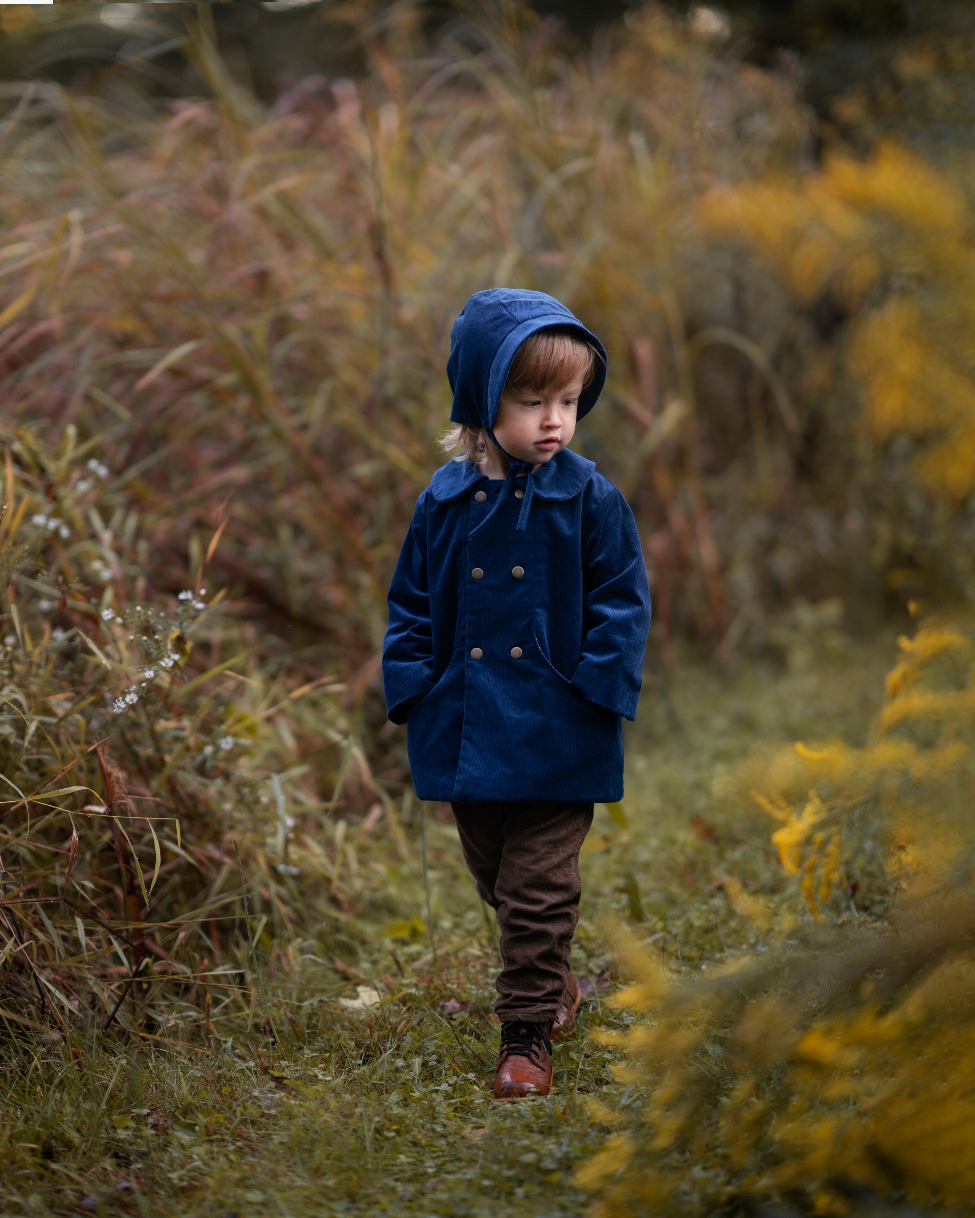 A 4-year-old model wearing the cornflower indigo blue corduroy bonnet alongside a matching coat, illustrating the perfect pairing for a stylish, coordinated look.