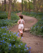 Child walking down a path in a forest with blue flowers on either side