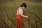 little boy in a field in orange overalls playing with a stick