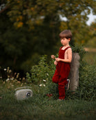 Child in red overalls standing next to a vintage radio in a natural setting