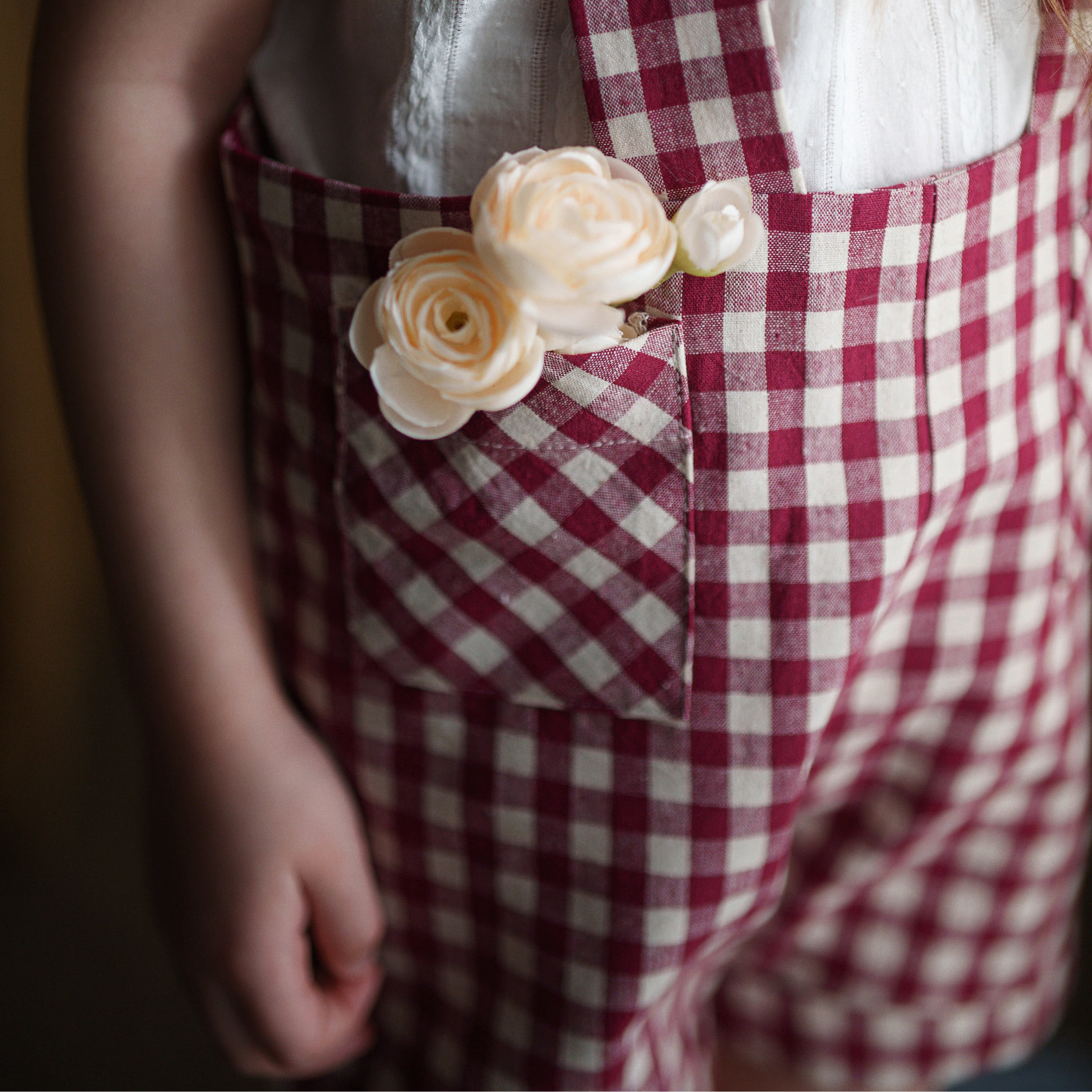 Child wearing red and white checkered overalls with floral details on a blurred background