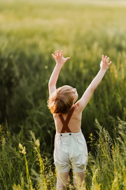 Boy seen from behind lifting arms and wearing natural short overalls