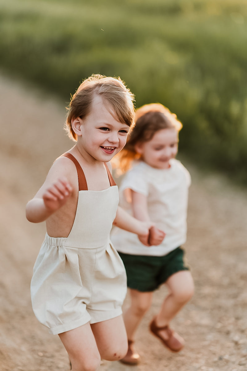 Boy and girl running hand in hand boy wearing natural short overalls