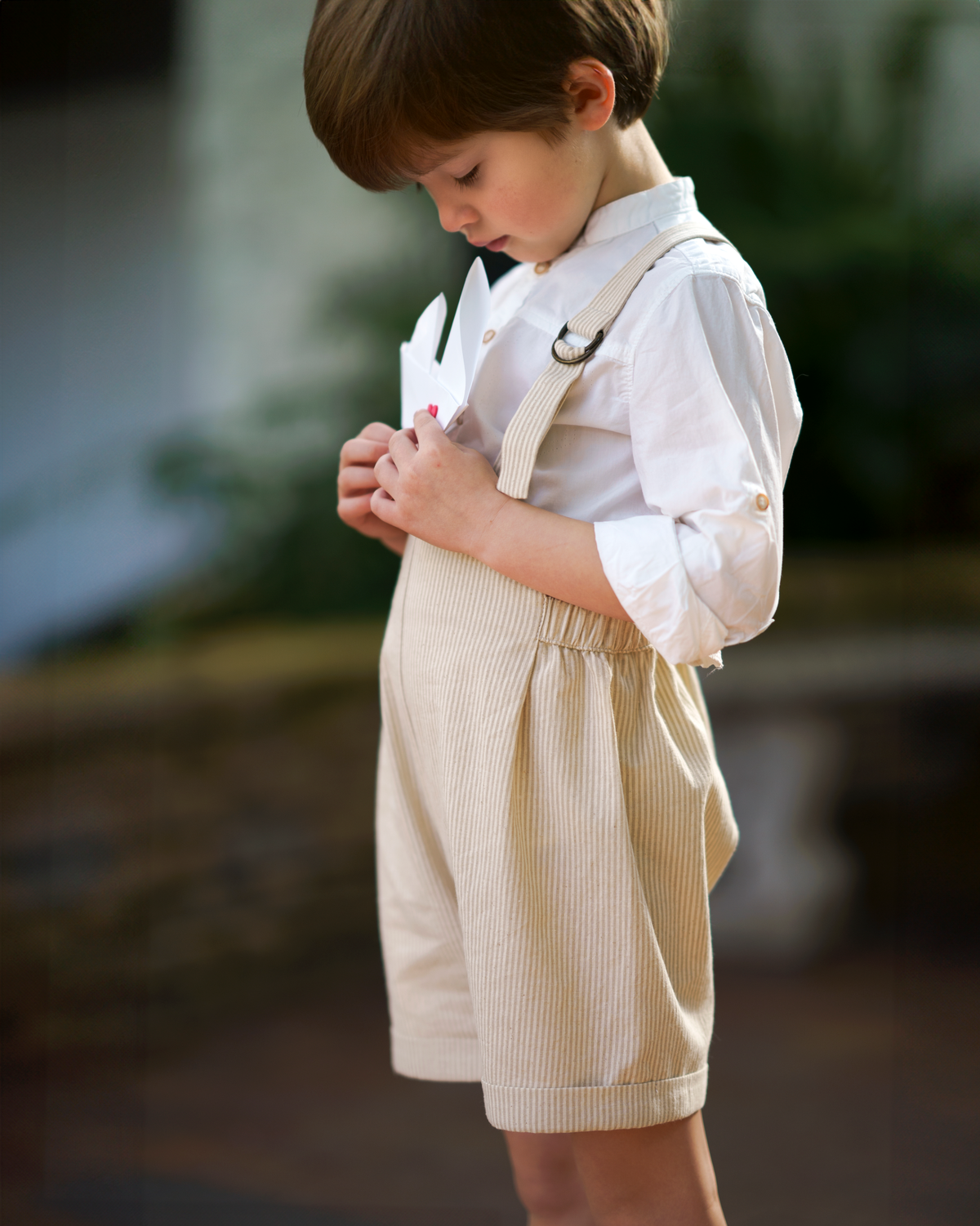 Little 5-year-old model wearing the Grow-With-Me Romper - Beige Stripes, showcasing the fully adjustable straps for a perfect fit, the classic timeless beige stripes pattern, and the comfortable, soft fabric ideal for all-day wear, embodying playful elegance in sustainable children's fashion.